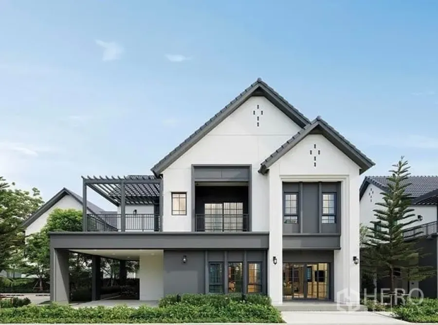 Detached House for sale in Bang Phli, Samut Prakan - Front elevation of the detached house with balcony, pergola terrace and driveway surrounded by greenery.
