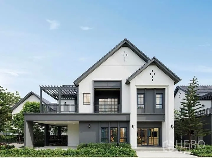 Detached House for sale in Bang Phli, Samut Prakan - Front elevation of the detached house with balcony, pergola terrace and driveway surrounded by greenery.