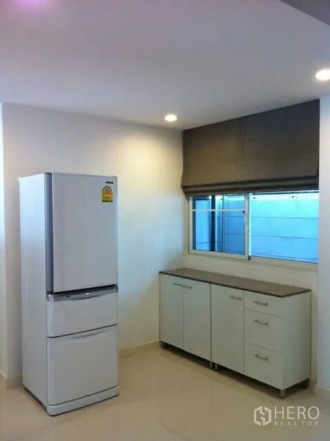 Townhouse for rent or sale in Suan Luang, Bangkok - Light kitchen corner with refrigerator, base cabinets and a window.