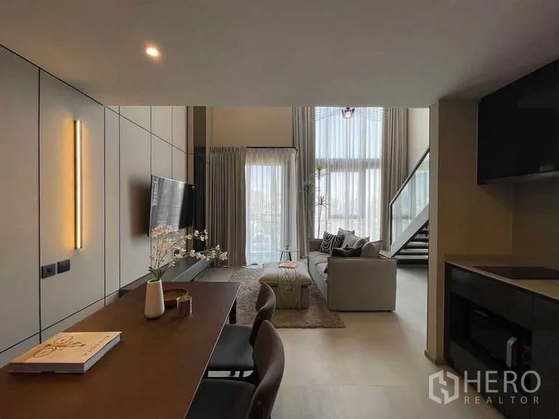 คอนโด ให้เช่าในPathum Wan, Bangkok - มุมมองจากห้องทานอาหารสู่ห้องรับแขก ผ้าม่านสูงจรดเพดาน ประตูกระจกออกระเบียง บันได และผนังทีวี