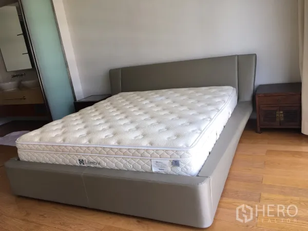 Condominium for rent in Khlong Toei, Bangkok - Master bedroom with upholstered platform bed and access to an ensuite bathroom.