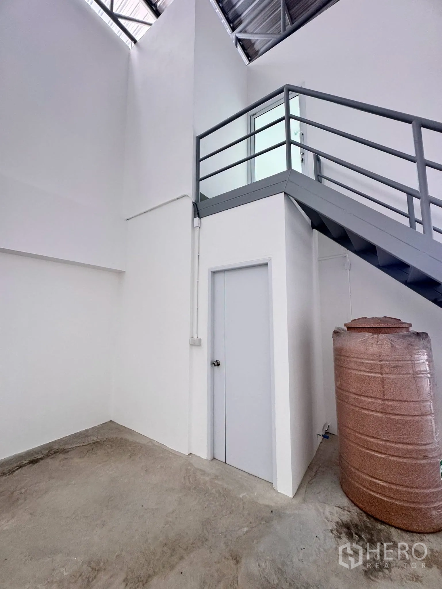 Warehouse for rent in Bang Bo, Samut Prakan - Ground corner with a metal staircase to the upper office and a water storage tank beside a door.