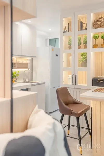 公寓 出售在Yan Nawa, Bangkok - 紧凑厨房视角，吧台配皮椅，白色高冰箱与带灯展示柜。