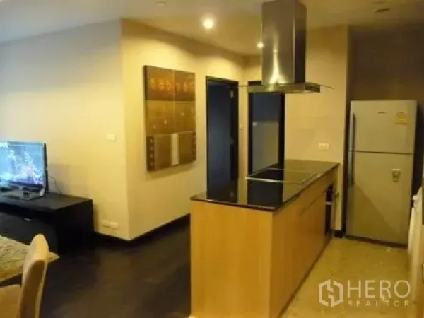 Condominium for rent in Sathon, Bangkok - Open-plan kitchen with island cooktop, stainless hood and fridge beside the living area.