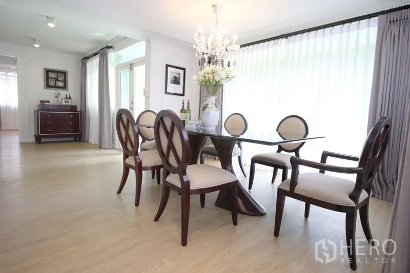 Detached House for rent in Chatuchak, Bangkok - Dining room featuring glass‑top table, six upholstered chairs, chandelier, and floor‑to‑ceiling curtains.