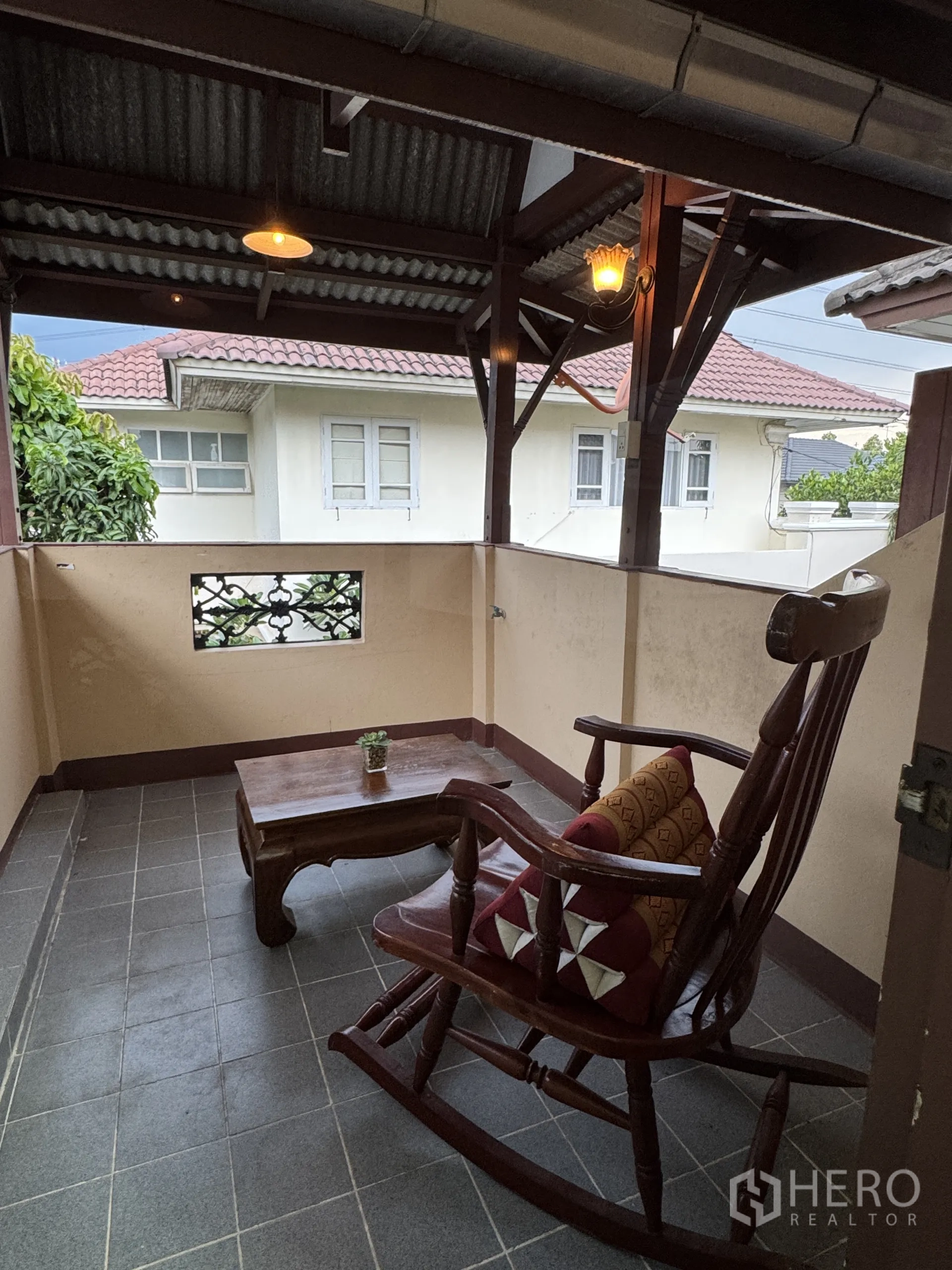 独立式住宅 出租在Min Buri, Bangkok - 二层有顶露台，摆放木质摇椅与茶几。