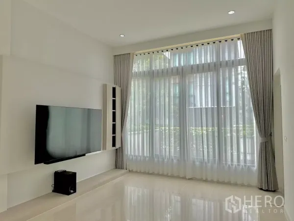 独立式住宅 出租或出售在Prawet, Bangkok - 挑高客厅采光充足，落地窗帘与壁挂电视。