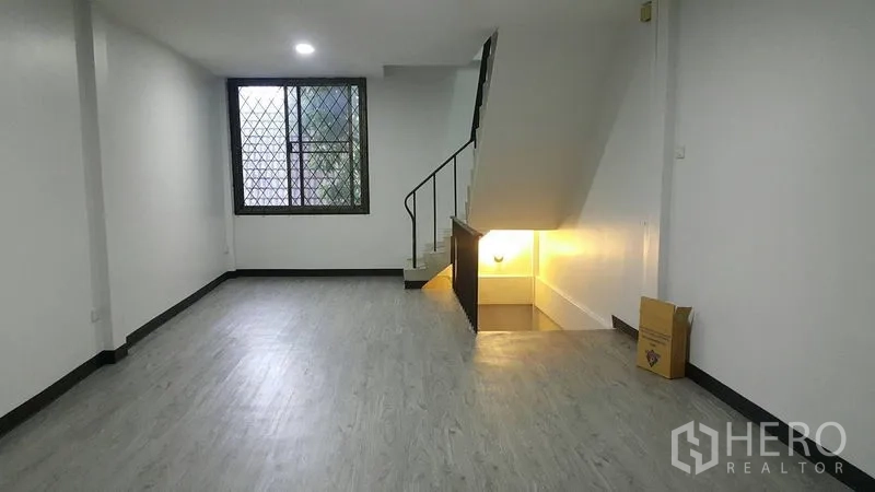 店屋 出租在Watthana, Bangkok - 一层开放式空间，木纹地板，带护栏窗与通往楼上的楼梯。