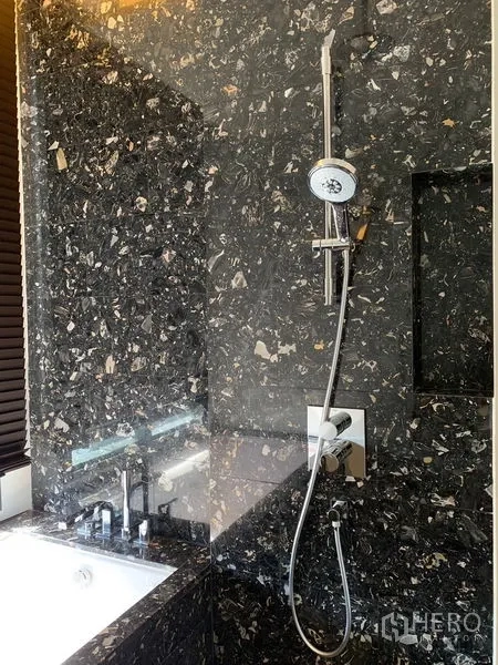 Condominium for rent in Khlong Toei, Bangkok - Bathroom with dark stone walls, bathtub, and rainfall handheld shower set.