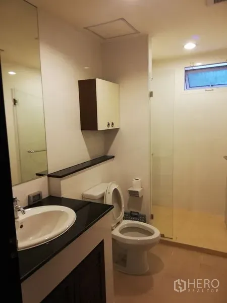 公寓 出租在Watthana, Bangkok - 现代化浴室，设大镜面台盆、马桶与玻璃淋浴间。