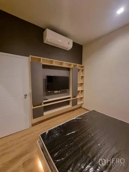 Townhouse for rent - Bedroom with built-in shelving and TV wall unit, air conditioner above and warm wood flooring.
