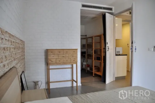 Condominium for rent in Bangkok - Bedroom corner with white brick walls, tall wooden chest and walk-in shelving next to the kitchen entrance.