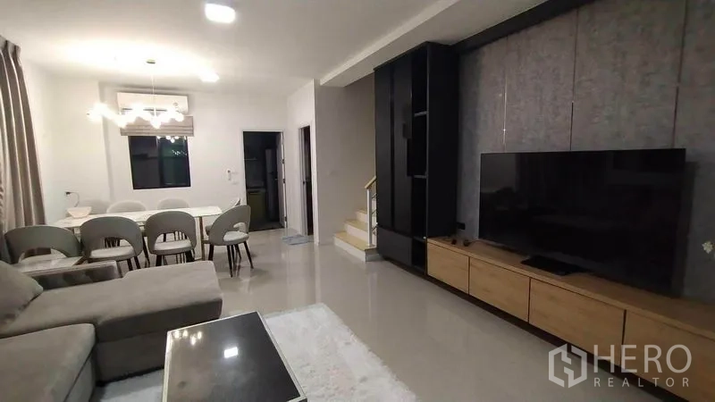 联排别墅 出租在Wang Thonglang, Bangkok - 开放式客餐厅，L型沙发、电视墙与楼梯，现代风联排别墅。