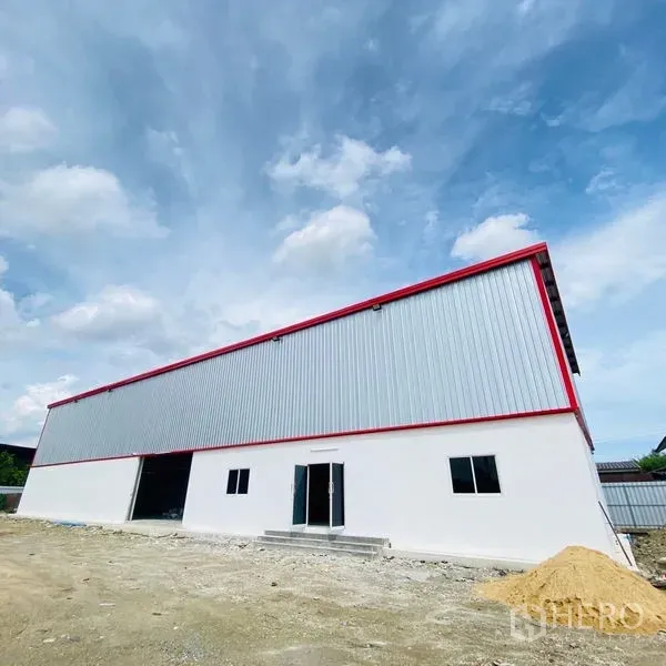 Warehouse for rent in Bang Khae, Bangkok - New-build warehouse exterior in Bang Khae with corrugated metal cladding, red trim, large loading door and open yard under blue sky.