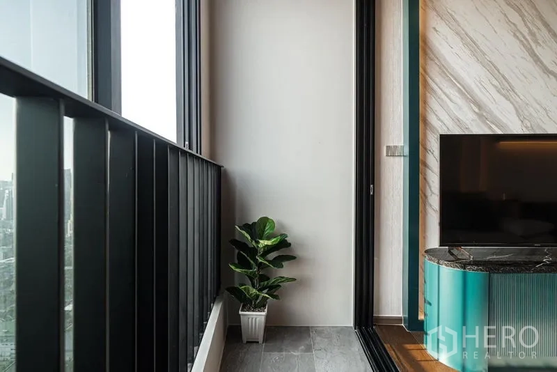 Condominium for rent in Khlong Toei, Bangkok - Slim balcony with a potted plant and sliding door beside the TV feature wall.