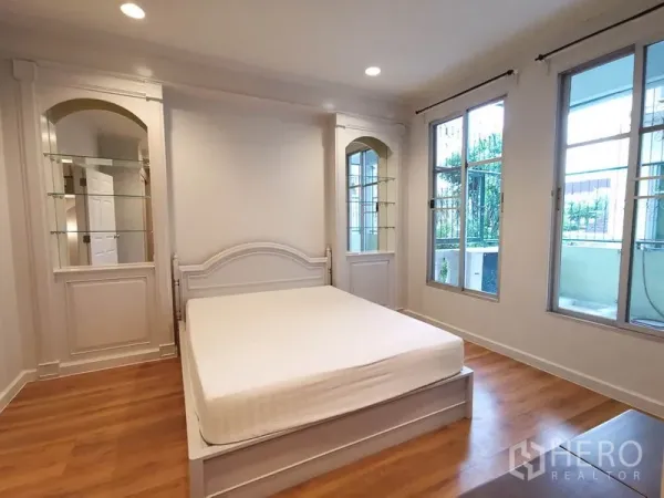 Townhouse for rent or sale in Yan Nawa, Bangkok - Second bedroom with wood flooring, built-in shelving and access to a balcony.