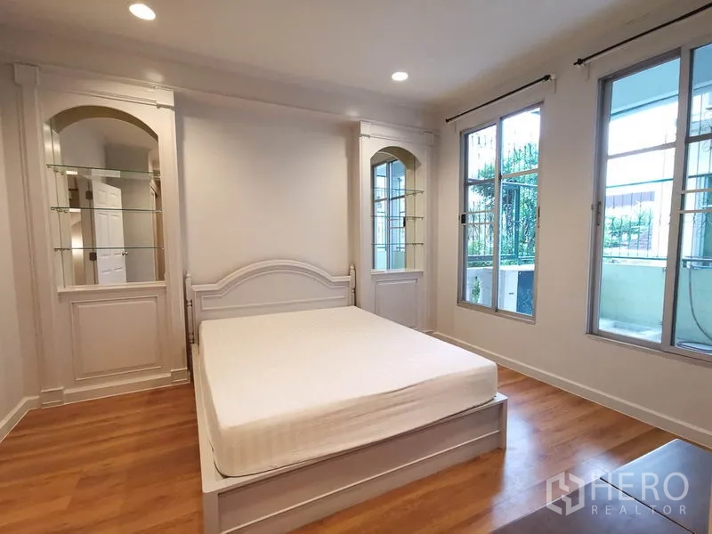 Townhouse for rent or sale in Yan Nawa, Bangkok - Second bedroom with wood flooring, built-in shelving and access to a balcony.