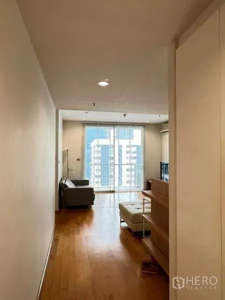 Condominium for rent in Ratchathewi, Bangkok - Bright hallway leading to a living room with wood floors, sofa, and balcony city view.