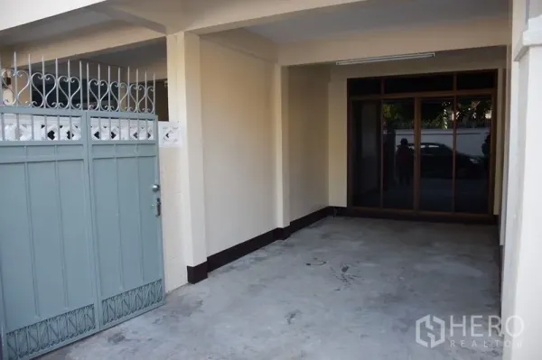 Townhouse for rent in Watthana, Bangkok - Covered carport behind sliding metal gate leading to glass entry doors.