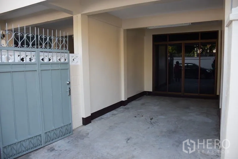 Townhouse for rent in Watthana, Bangkok - Covered carport behind sliding metal gate leading to glass entry doors.