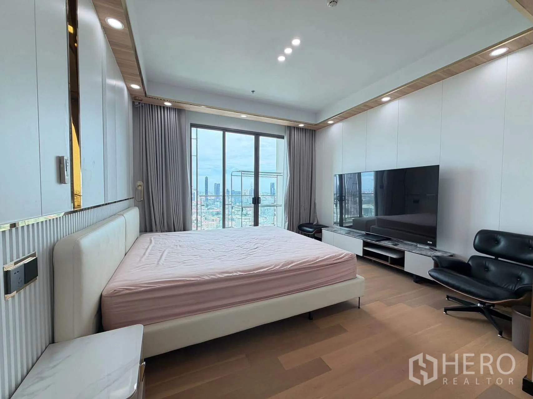Condominium for sale in Watthana, Bangkok - Bedroom with large TV console, lounge chair, and panoramic window.