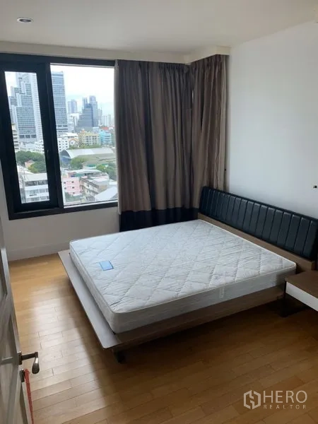 Condominium for rent or sale in Khlong Toei, Bangkok - Bedroom with large window and city skyline view, wood flooring and a platform bed frame.