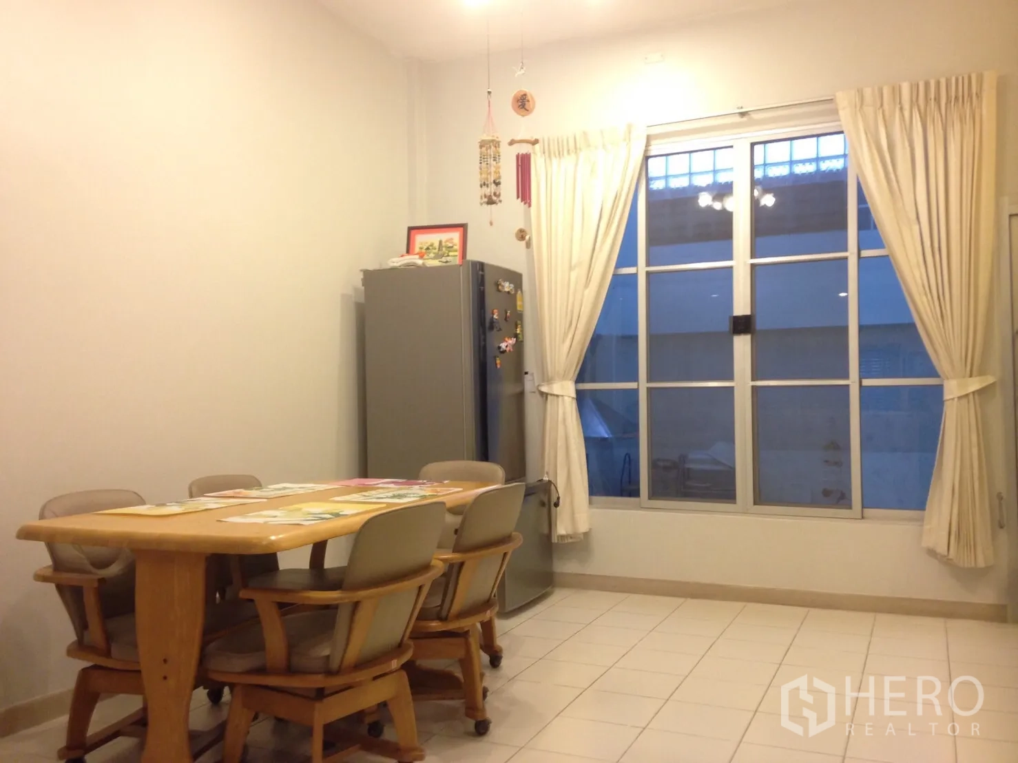 联排别墅 出租在Wang Thonglang, Bangkok - 明亮餐区，六人木桌、瓷砖地面和大窗帘窗。