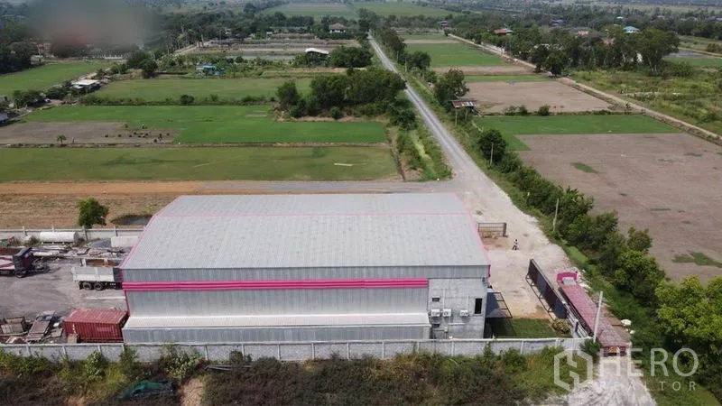 Warehouse for sale in Lam Luk Ka, Pathum Thani - Aerial view of the warehouse compound with perimeter wall, rural fields and an access road.