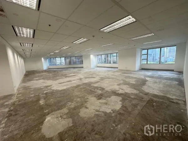 Office Space for rent - Large open-plan office floor with unfinished concrete subfloor, grid ceiling lighting and wide windows with city outlook.
