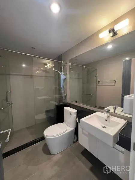 公寓 出租在Ratchathewi, Bangkok - 现代卫浴，玻璃淋浴间、洗手台与马桶，灯光温暖。