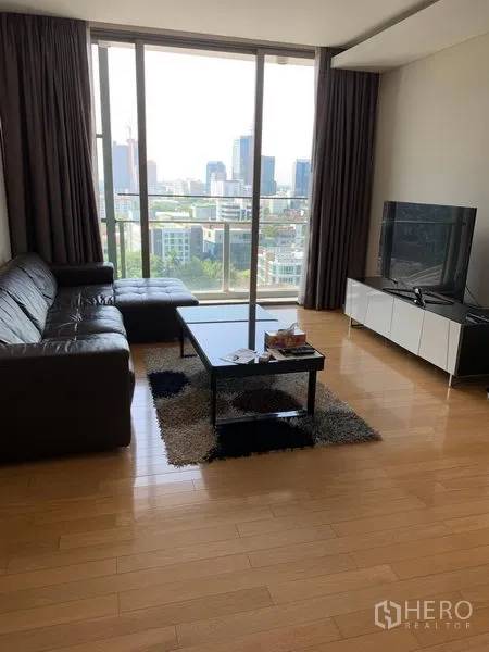 公寓 出租在Watthana, Bangkok - 客厅配皮沙发与电视柜，落地窗可赏曼谷城市天际线。