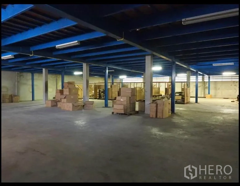 Warehouse for rent in Nakhon Pathom - Large storage area under blue mezzanine-style structure with pillars and cartons on the floor.