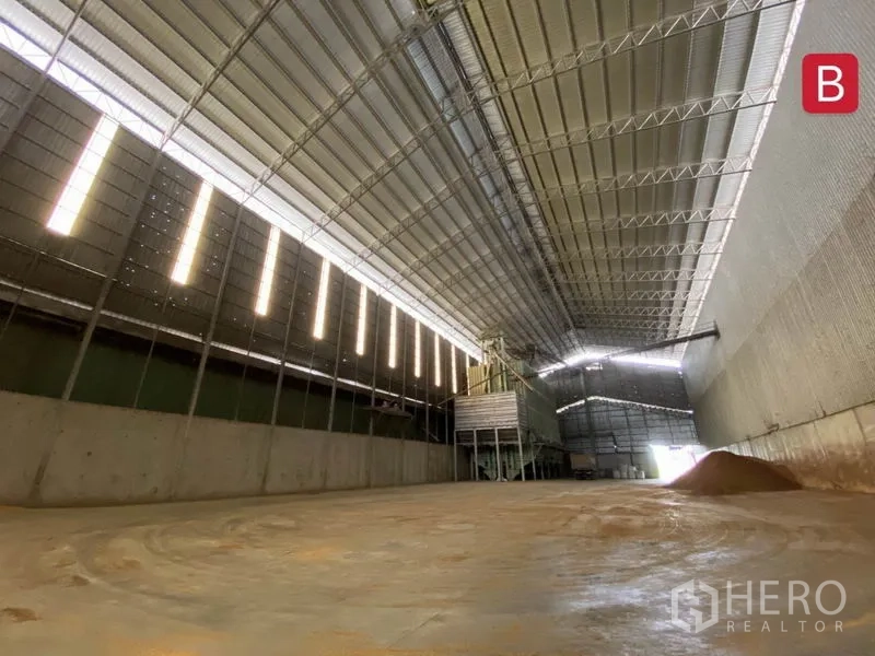 Factory for rent in Chachoengsao - Large covered storage area featuring skylight strips, high truss roof, and concrete retaining walls.