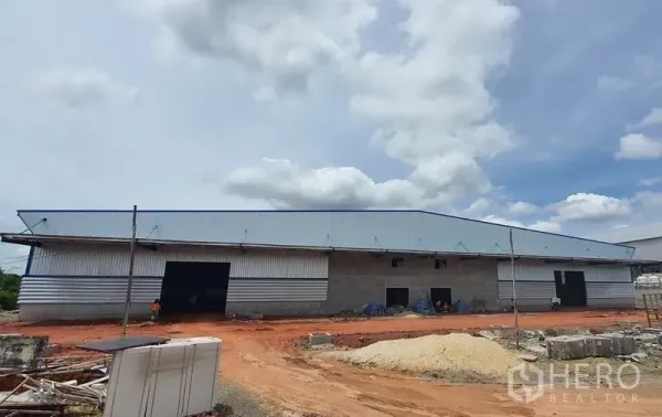 Warehouse for rent in Mueang Samut Sakhon, Samut Sakhon - Front elevation of a long warehouse with multiple roller-shutter loading bays and construction materials on site.