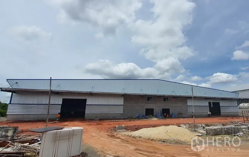 Warehouse for rent in Mueang Samut Sakhon, Samut Sakhon - Front elevation of a long warehouse with multiple roller-shutter loading bays and construction materials on site.