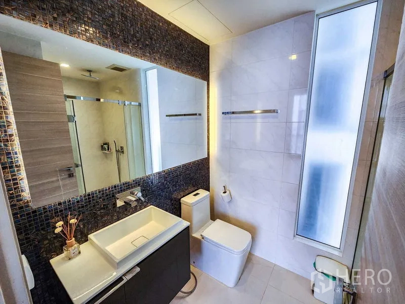 Condominium for rent or sale in Bang Rak, Bangkok - Contemporary bathroom with a backlit mirror, vanity, and frosted window.
