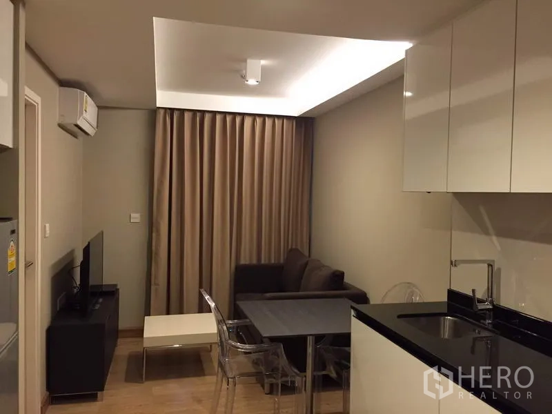 คอนโด ให้เช่าในWatthana, Bangkok - มุมนั่งเล่นมีโซฟา ทีวี โต๊ะทานอาหาร และไฟซ่อนฝ้า ถัดจากตู้ครัวสีขาวเงา