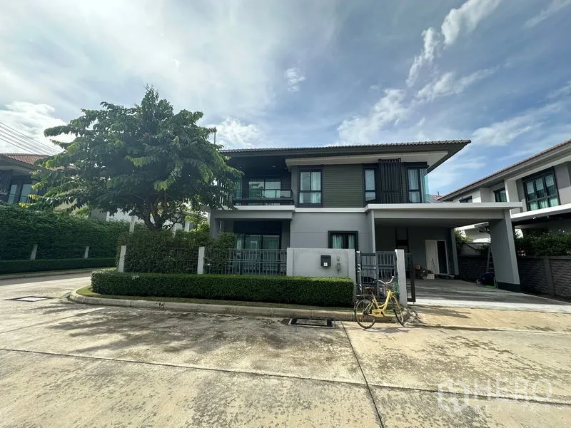 Detached House for rent in Lam Luk Ka, Pathum Thani - Front façade of modern two-storey home with mature tree and low hedges.