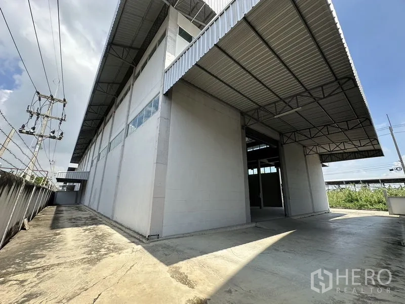 Factory for rent in Lam Luk Ka, Pathum Thani - Rear driveway and loading area with deep canopy attached to the factory wall.