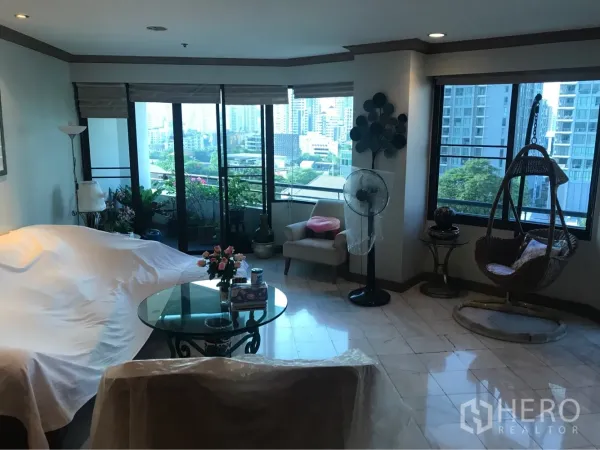 Condominium for rent or sale in Watthana, Bangkok - Spacious living room with tiled floors, glass coffee table, sliding doors to a balcony, and skyline views near Ekkamai.