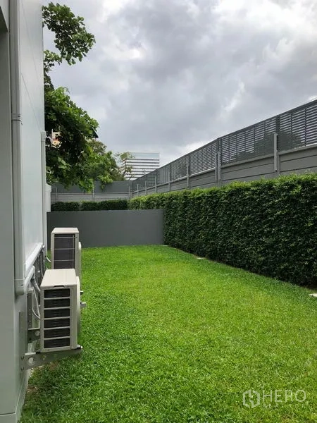 独立式住宅 出租在Watthana, Bangkok - 侧院草坪整洁，绿篱与私密围栏，并列外机。
