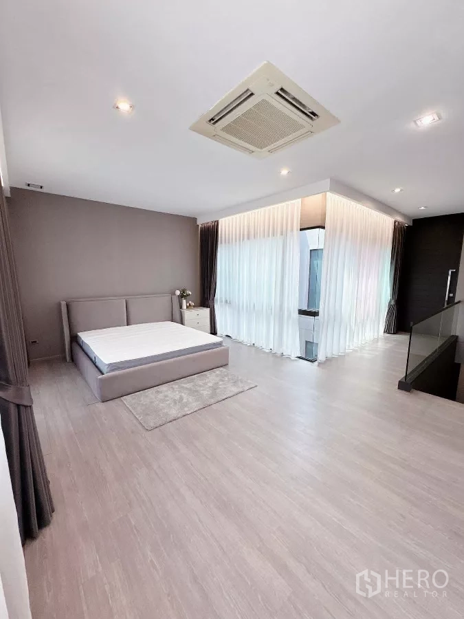 Townhouse for rent or sale in Lat Phrao, Bangkok - Expansive master bedroom with corner glass and full-height curtains.