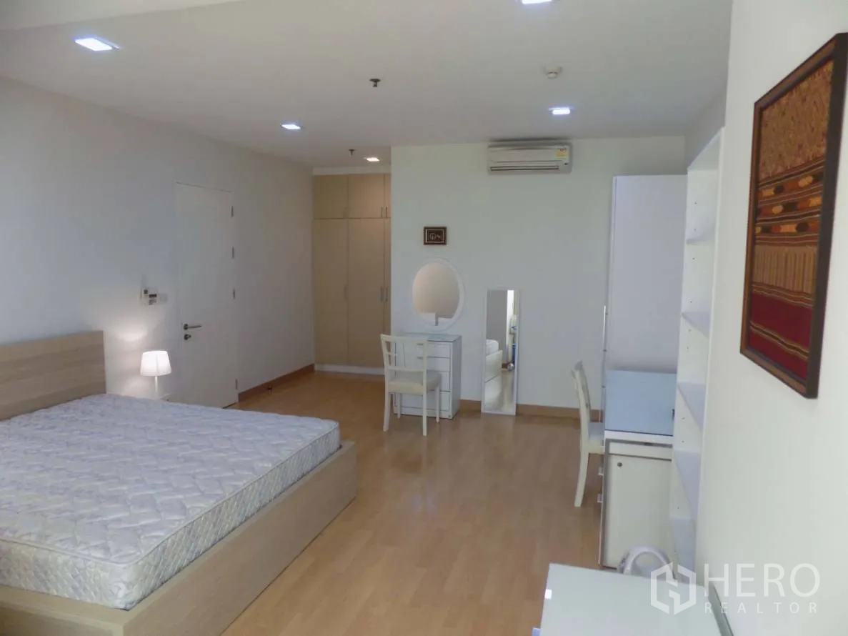 Condominium for rent or sale in Khlong Toei, Bangkok - Spacious bedroom with queen bed, wood floors, study desk, vanity and built-in wardrobe with air conditioning.