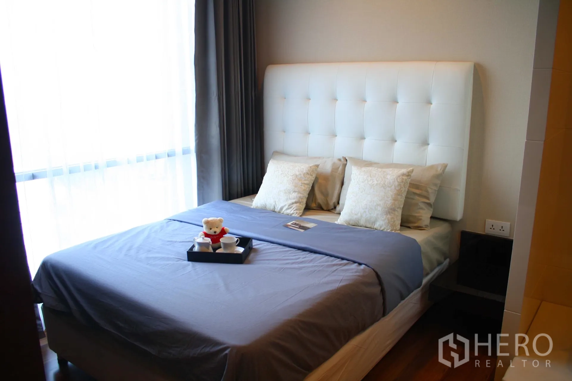 Condominium for rent in Huai Khwang, Bangkok - Cozy bedroom with a tufted white headboard, soft pillows, and a large curtained window bringing natural light.