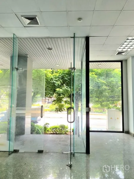 零售空间 出租在Sathon, Bangkok - 店内玻璃双开门入口，可见外部绿树成荫的人行道。