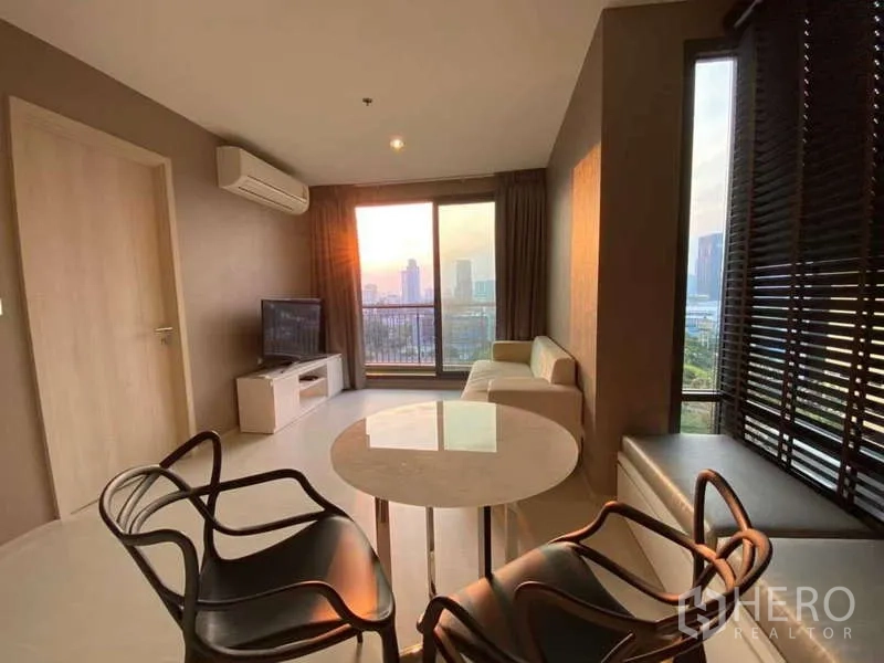 Condominium for rent or sale in Khlong Toei, Bangkok - Living room seating and round table beside full‑height windows showcasing sunset city views.