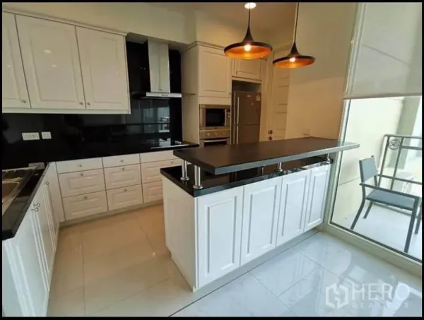 Condominium for rent in Watthana, Bangkok - Modern white kitchen with island bar, black countertops, and balcony access.