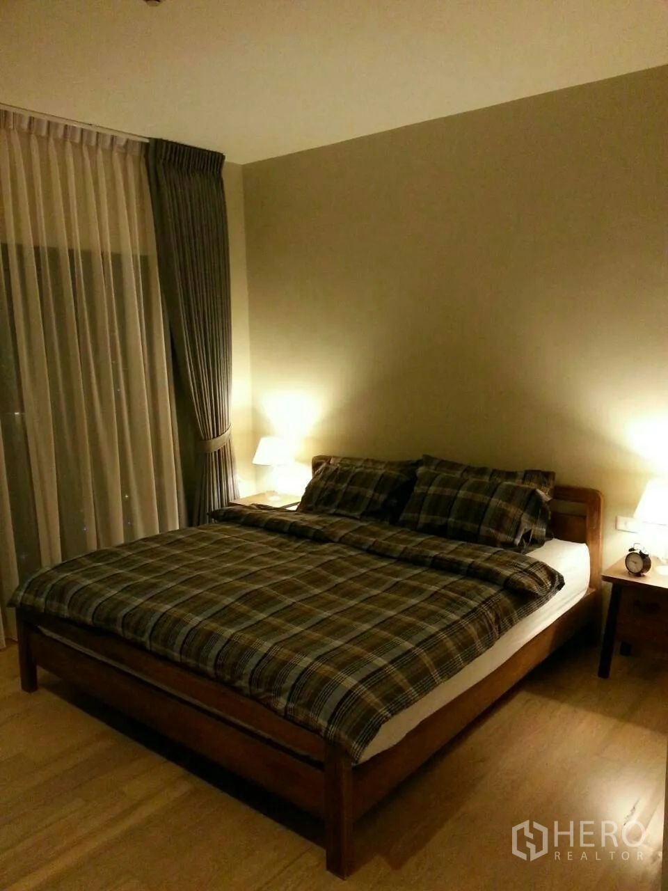 Condominium for rent or sale in Watthana, Bangkok - Warm‑lit bedroom with queen bed, plaid bedding, nightstands and large window with double curtains.