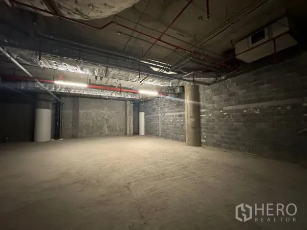 Retail Space for rent - Unfitted retail interior with high ceiling, lighting strips, red sprinkler pipes and structural columns.