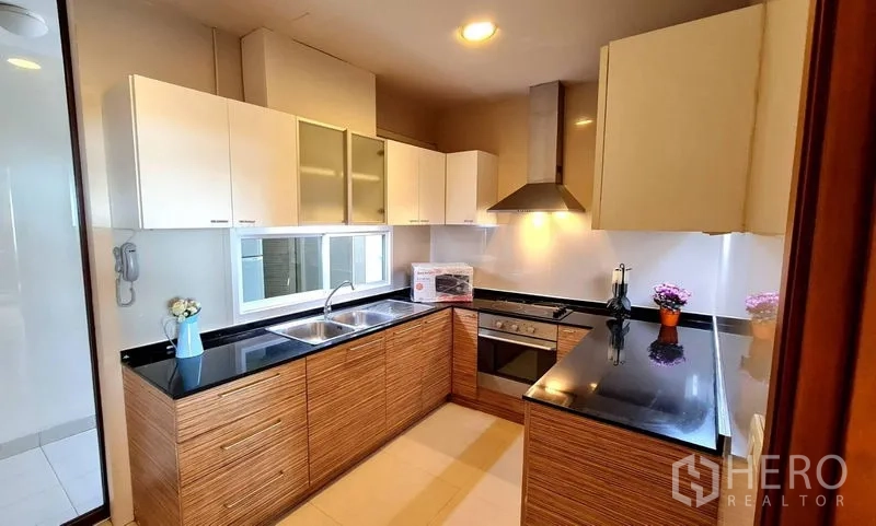 Apartment for rent in Khlong Toei, Bangkok - Closed kitchen with black granite counters, oven, hood and double sink.